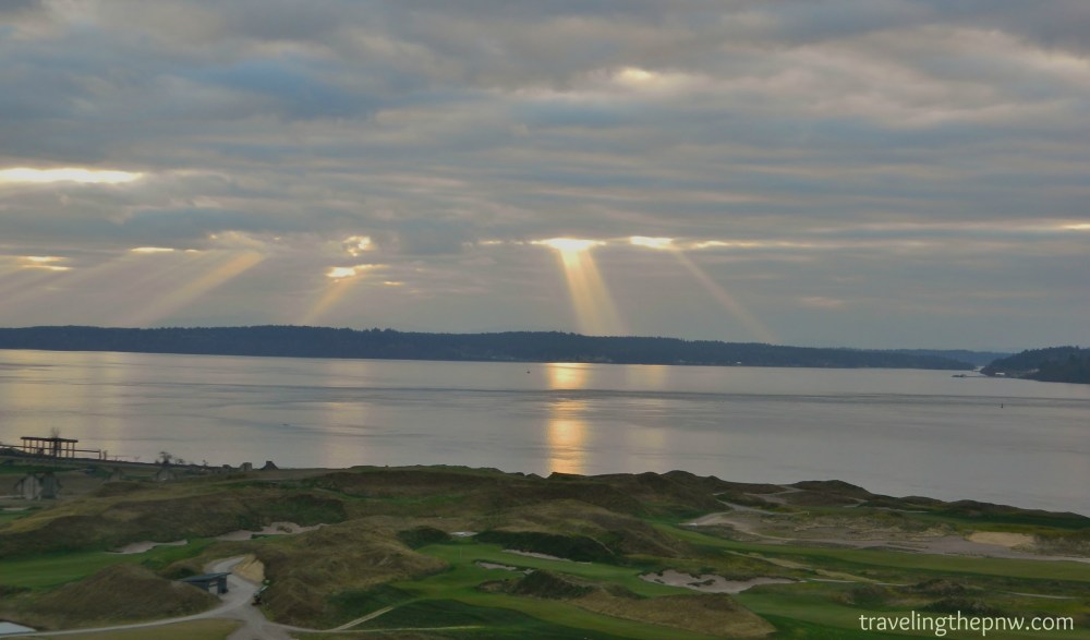 Sun rays pour over the Puget Sound with the Chambers Bay Golf Course in the foreground.